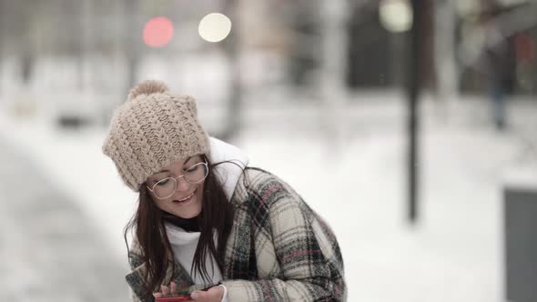 Cheerful Brunette Woman Is Walking at Winter Park Listening To Music By Cell Phone and Singing Song