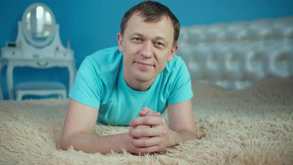 Smiling young man lying on bed in bedroom and looking at camera