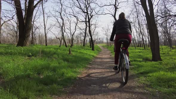 Young Woman on a Bicycle Rides Along a Path in the Forest in a Sunny Spring Day