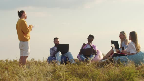 Field Four People are Sitting in Chair Bags the Grass with Laptops Their Knees Listening to Their