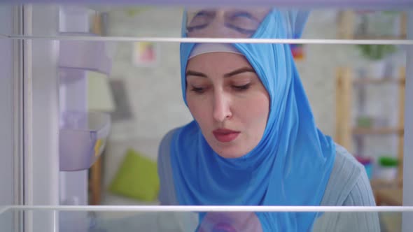 Young Muslim Woman in a National Headscarf Looks Into the Empty Refrigerator