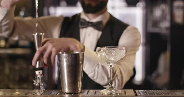 Close-up Shooting. The Bartender Is Pouring Alcohol From a Bottle Into a Shaker Using a Measuring