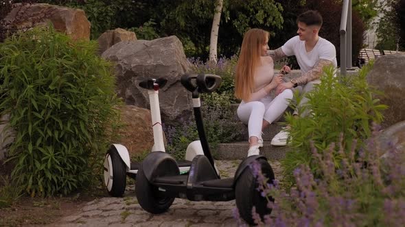 Couple Are Sitting on Stones in the Park,their Gyro Scooters Are Standing Nearby