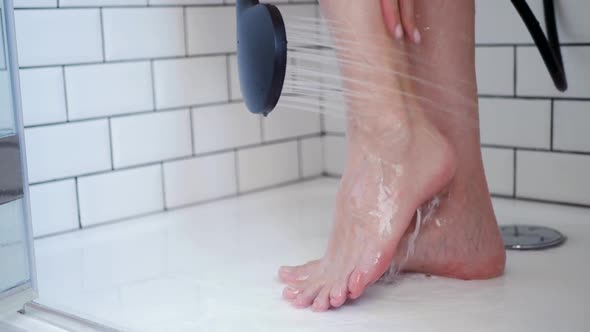 Woman Washes Her Feet with a Black Shower in a White Bathroom