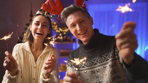 Happy Smiling Couple Woman in Festive Elf Cap and Man in Red Reindeer Antlers Headband Looking at