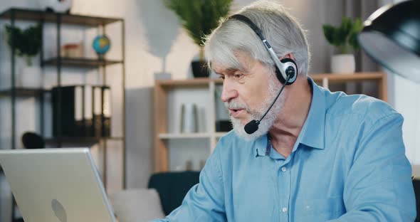 Old Man Using Laptop and Headset for Video Conversation