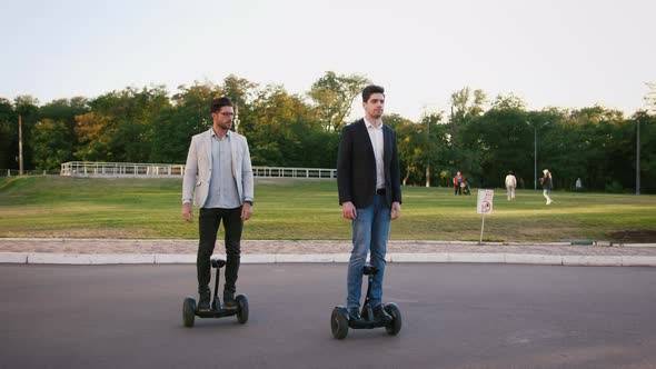 Two Elegant Businessmen Riding Hoverboard in City Park on Sunny Day Slow Motion