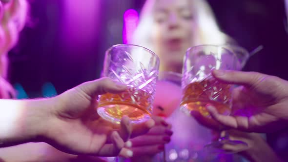 Closeup Clinking Glasses of Blurred Group of Friends in Night Club Lights