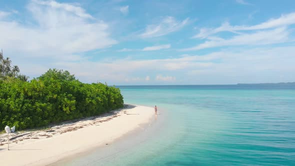 Aerial slow motion: lady walking on tropical beach at sunset, away from it all