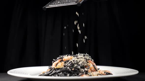 Chef Grating Hard Cheese on Freshlycooked Black Seafood Pasta