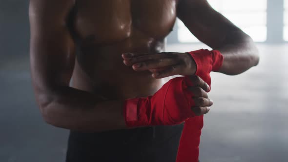 Shirtless african american man wrapping hands for boxing in an empty urban building