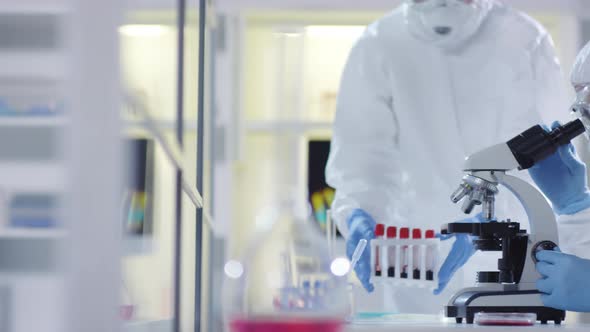 Medical Scientist in Protective Suit Looking into Microscope alt