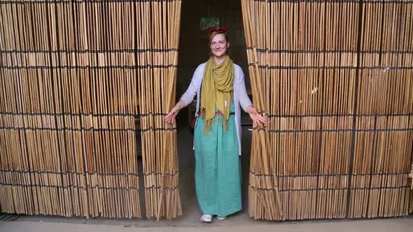 Young happy woman opening curtain made of palm