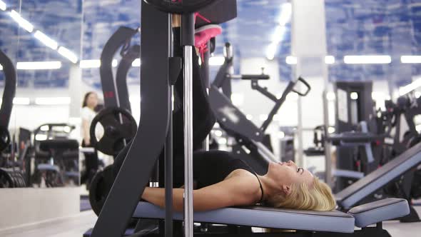 Attractive Young Blond Caucasian Woman with Sporty Body Smiling While Exercising on Leg Press