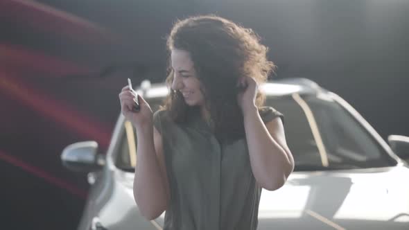 Portrait of Happy Caucasian Brunette Woman Bragging Car Keys in Dealership. Excited Young Girl with