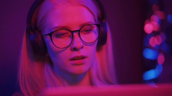 Close Up of Young Caucasian Teenage Girl Wearing Earphones and Eyeglasses Sitting in Front of PC