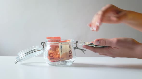 Women's hands count and put a euro bill in a glass jar. Close-up.