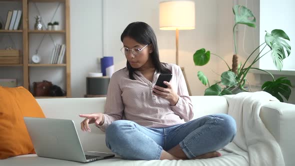 Businesswoman Using Smartphone and Laptop Sitting on Couch in Home Room Spbd