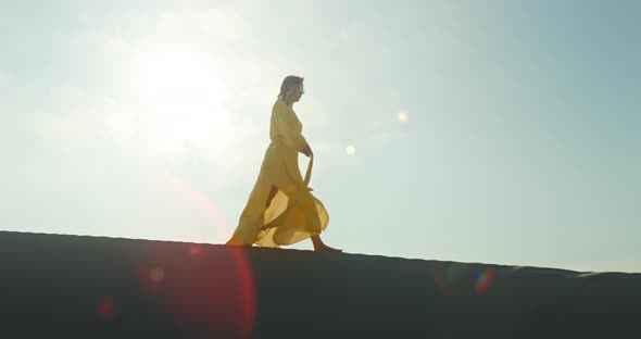 Stylish Woman in Yellow Dress Walking on Top of Sand Dune in Slow Motion