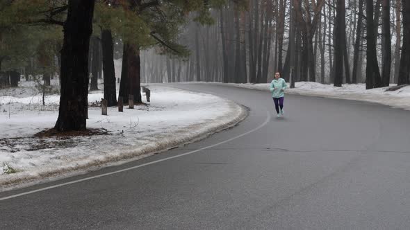 Senior old Caucasian woman running in the snowy park in winter with headphones.