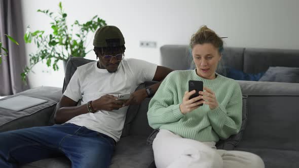 Happy Biracial Couple Relaxing on Sofa with Smartphones