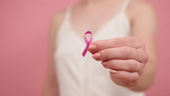 Close Up, Woman Holding Silk Pink Ribbon Between Her Fingers. Breast Cancer Awareness Month Pink