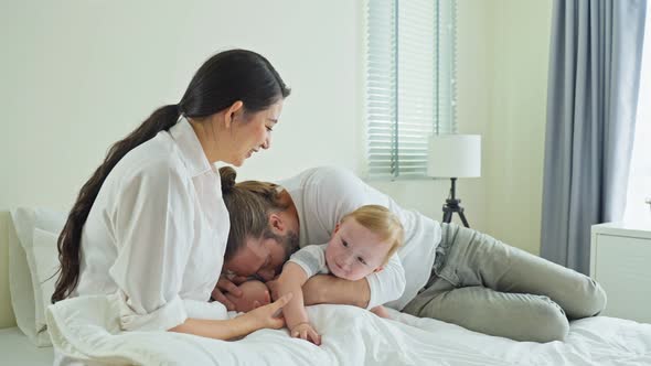 Caucasian loving parents play with baby boy child on bed in bedroom.