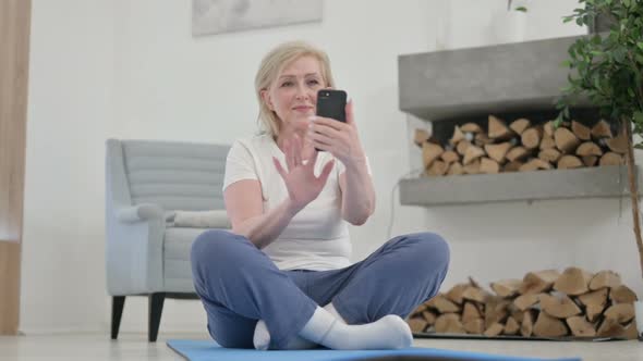 Old Woman Using Smartphone on Yoga Mat at Home