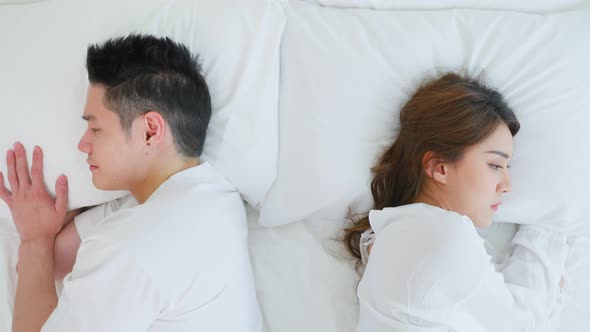 Asian young couple lying down on bed with painful after fight argument.