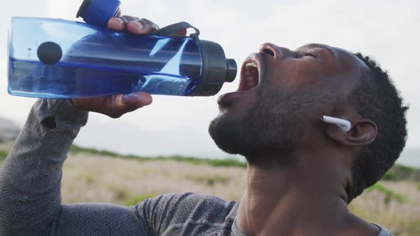 African american man drinking water from bottle while hiking in the mountains