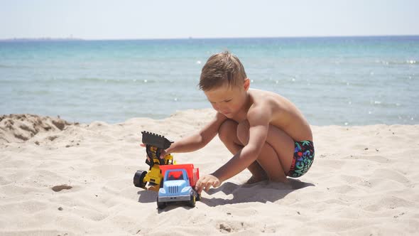 Cute Boy Playing with Sand and Plastic Cars, Toys on the Shore of the Azure Sea