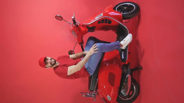 Portrait of a Smiling Courier in Uniform Sitting on a Scooter, Isolated Red Background