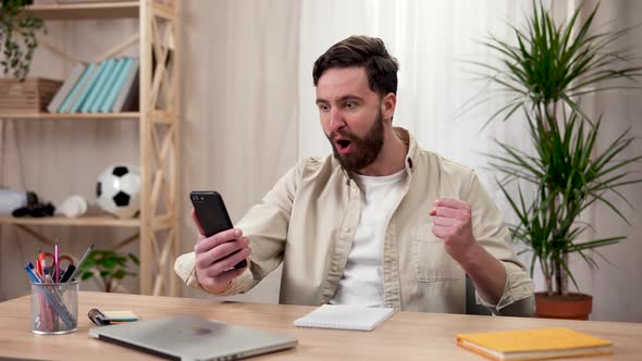 A Man Watches an Online Sports Game on His Smartphone Shouts a Goal and Celebrates a Victory