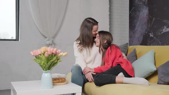 Mother Hug and Kiss Her Daughter While They are Sitting on Sofa and Talking
