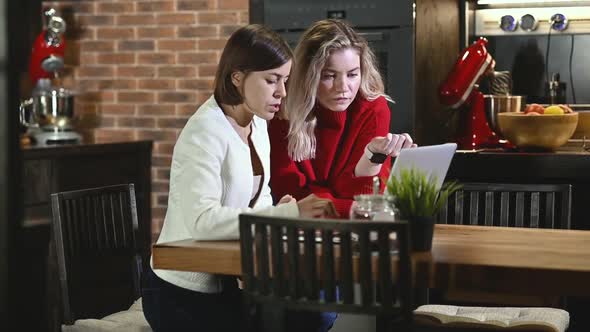 Two girls are working in kitchen at home with laptop table discussing project