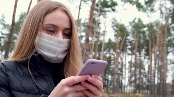 Young Blond Woman Wearing Protective Mask Talking on Phone Outside in the Park