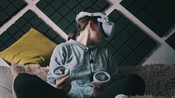 Young Woman Sitting on Sofa Playing Game Using VR Helmet Indoor at Home