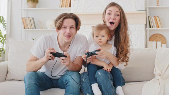 Caucasian Family Playing Video Game Console at Home Sitting on Sofa Young Mother and Little Daughter