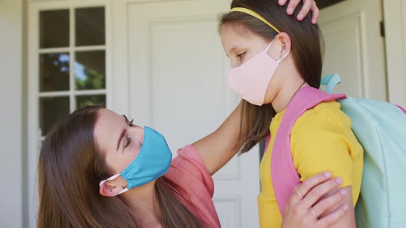 Caucasian mother wearing face mask embracing her daughter outside of the house