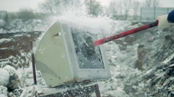 White TV Is Smashed with Hammer at a Landfill. Man with a Hammer Shatters the TV Screen.