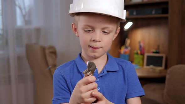 Portrait of a Small Surprised Boy in a Helmet with Tools in His Hands at Home