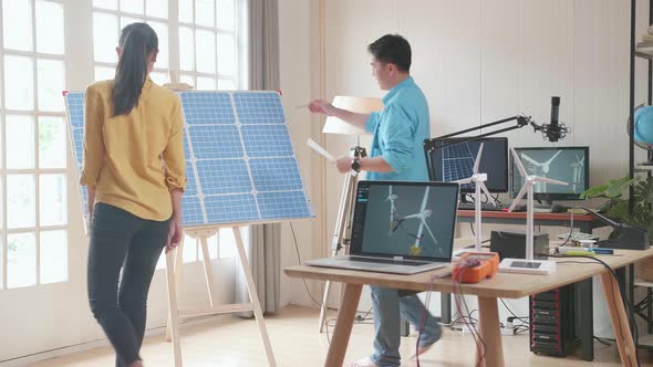 Asian Man And Woman Discuss Work With Solar Cell Panel And Laptop Computer Showing Wind Turbine