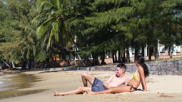 Interracial Pregnant Young Couple Lying on the Sand in the Beach on a Sunny Day