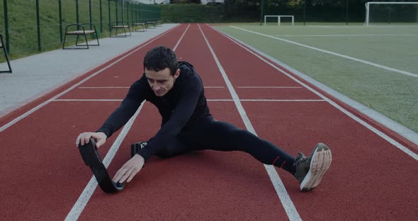 Male Disabled Sportsman with Prosthetic Running Blades Stretching Back While Sitting at Sports Field
