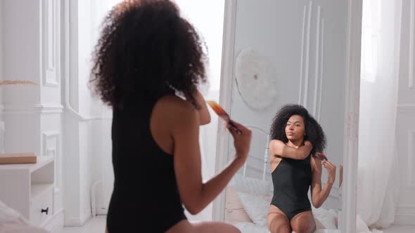 Black Woman Combing Her Afro Hair Sitting on a Bed and Looking in Mirror