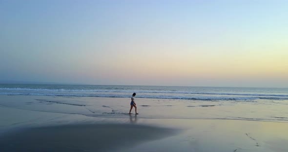 Aerial drone view of a young woman walking on the beach at sunset.