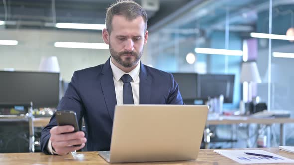 Young Businessman Using Smartphone and Laptop in Office