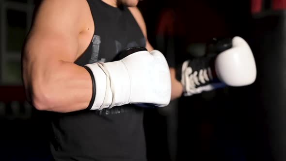 Muscular Man in Black Clothes Puts on Leather White Boxing Gloves on His Hands Before a Competition