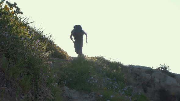 Young man running up hill towards sunlight at golden hour