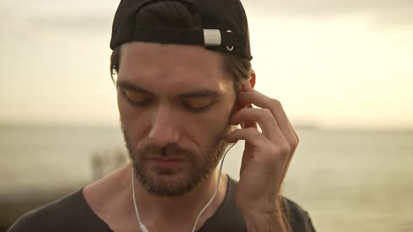 Closeup Caucasian Bearded Man with Cap on Backward Listening Music Using Headphones Early in Morning